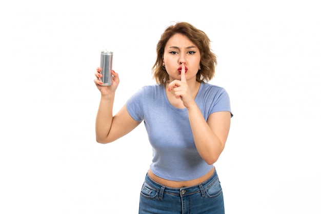 A front view young attractive lady in grey t-shirt and blue jeans holding silver can showing silence sign on the white