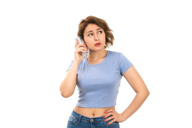 A front view young attractive lady in grey t-shirt and blue jeans holding silver can talking through it on the white