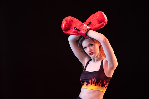 A front view young attractive lady in red boxing gloves fire shirt on the black background sport boxing training