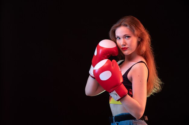 A front view young attractive lady in red boxing gloves fire shirt on the black background sport boxing training