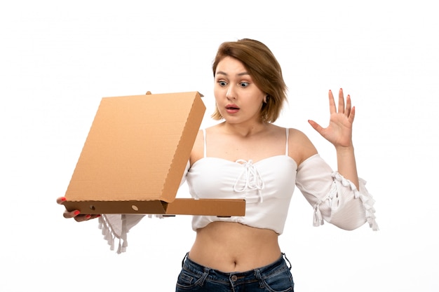 A front view young attractive lady in white shirt and blue jeans holding brown package opening it badly surprised on the white