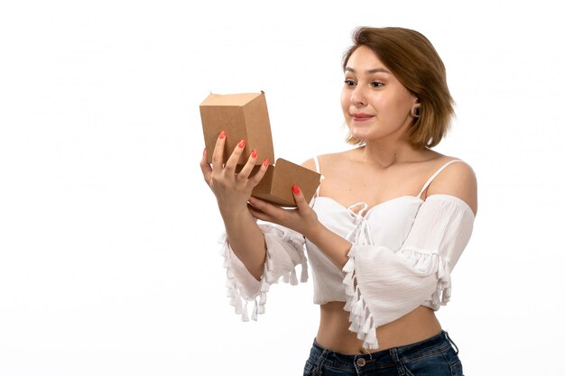 Free photo a front view young attractive lady in white shirt and blue jeans holding brown package opening it happy on the white