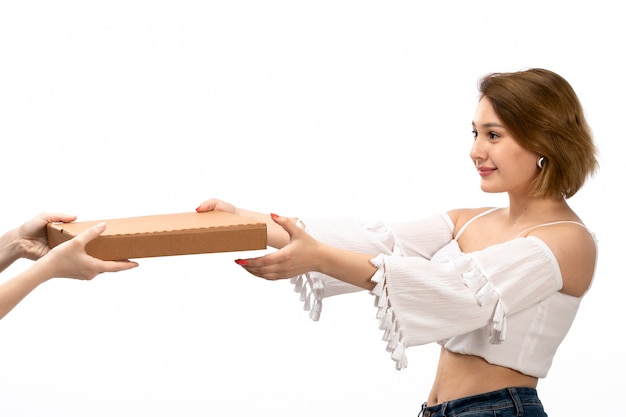 A front view young attractive lady in white shirt and blue jeans taking brown package on the white