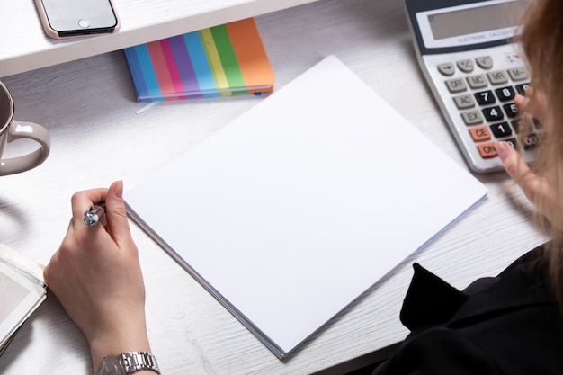 Free photo a front view young attractive lady working with documents in front of table with calculators cup phone light background work business technologies