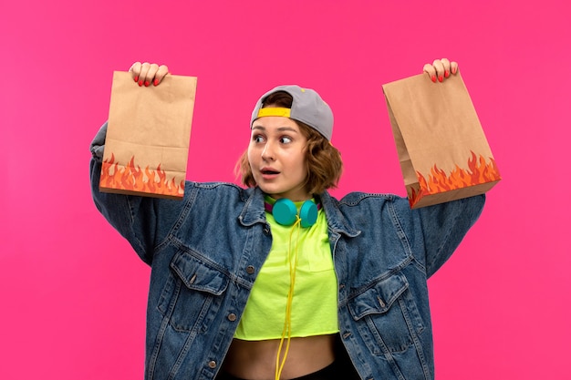 Free photo a front view young attractive woman in acid colored shirt black trousers jean coat holding brown box colorful bag on the pink background young female fashion