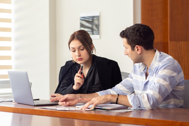 A front view young beautiful businesswoman in black shirt black jacket along with young man discussing work issues inside her office work job building
