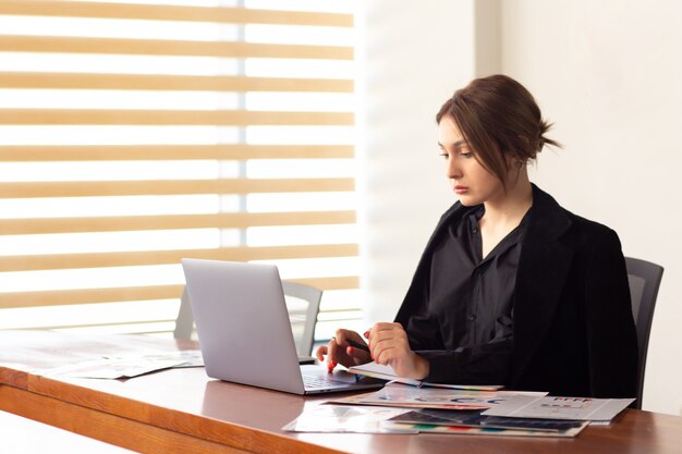 A front view young beautiful businesswoman in black shirt black jacket using her silver laptop writing reading working inside her office work job building