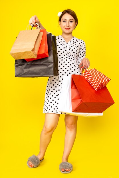 A front view young beautiful female in black and white polka dot dress holding shopping packages on yellow