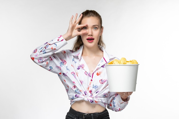 Front view young beautiful female eating potato cips and watching movie on a white surface