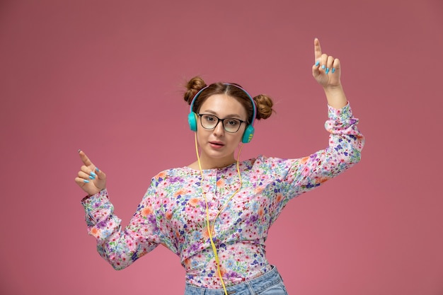 Free photo front view young beautiful female in flower designed shirt and blue jeans dancing and listening to music on pink background