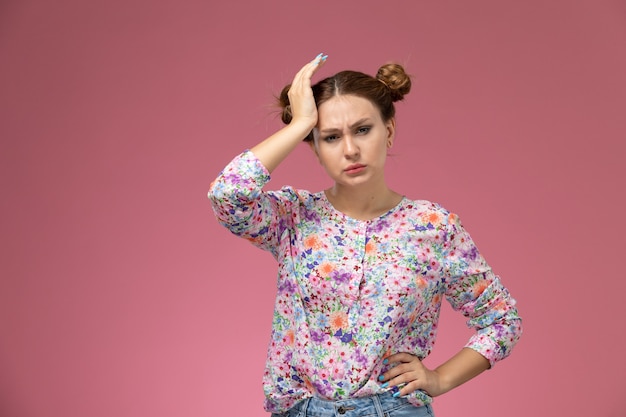 Front view young beautiful female in flower designed shirt and blue jeans having headache on the pink background