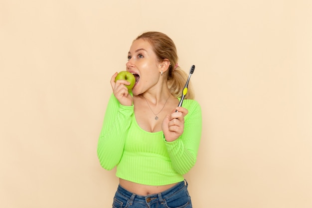 クリーム色の壁に青リンゴを食べる緑のシャツを着た若い美しい女性の正面図フルーツモデル女性まろやかな