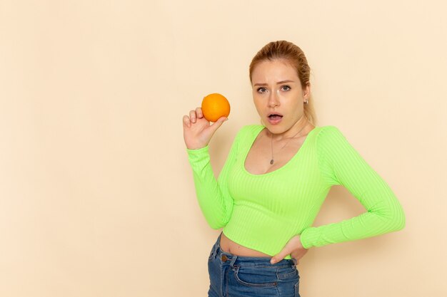 Front view young beautiful female in green shirt holding fresh orange on cream wall fruit model woman mellow