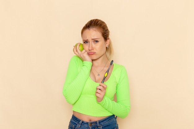 Free photo front view young beautiful female in green shirt holding green apple on the cream wall fruit model woman mellow