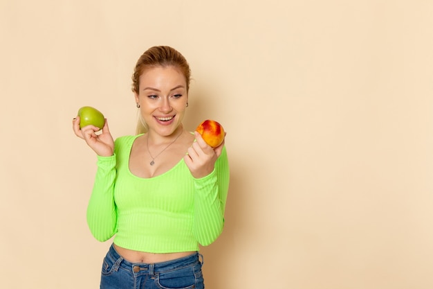 Front view young beautiful female in green shirt holding pair of fresh apples on cream wall fruit model woman mellow