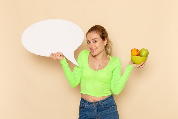 Front view young beautiful female in green shirt holding plate full of fruits with white sign on cream wall fruit model woman vitamine