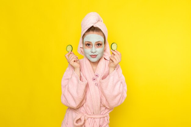 A front view young beautiful female in pink bathrobe holding cucumber