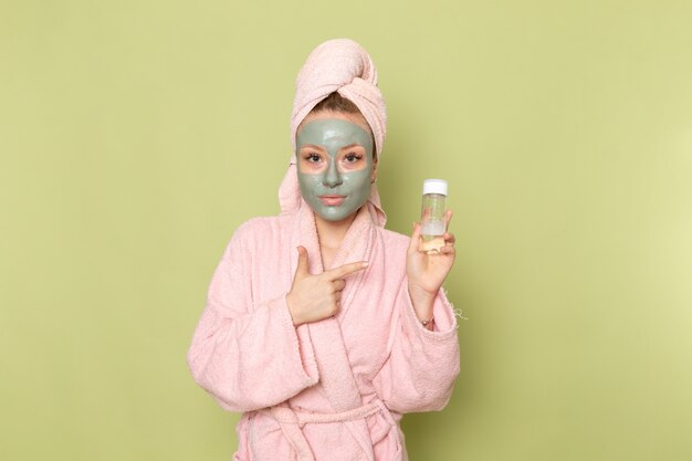 A front view young beautiful female in pink bathrobe holding spray flask