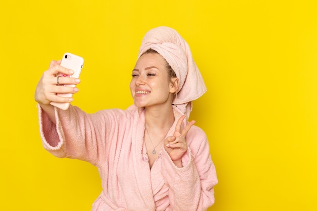 A front view young beautiful female in pink bathrobe taking a selfie