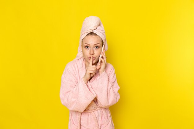 A front view young beautiful female in pink bathrobe talkign on the phone quietly