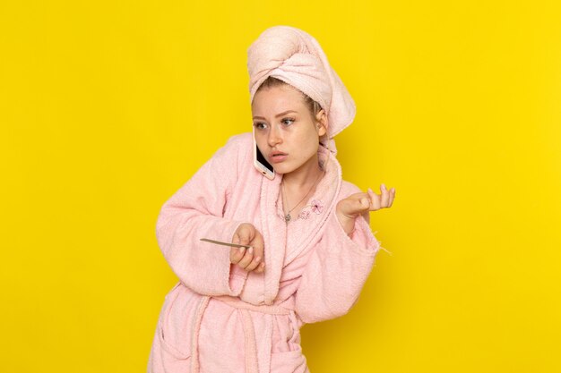 A front view young beautiful female in pink bathrobe talking on the phone