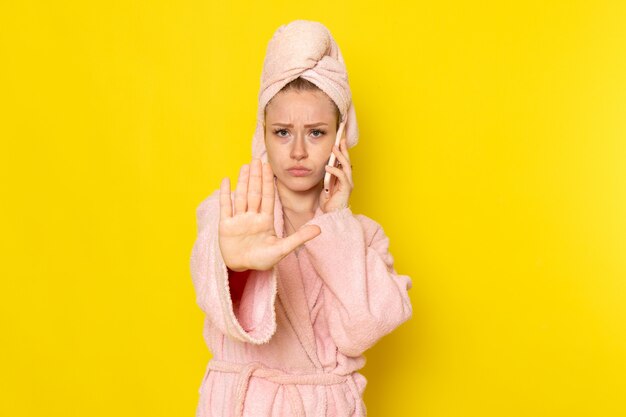 A front view young beautiful female in pink bathrobe talking on the phone