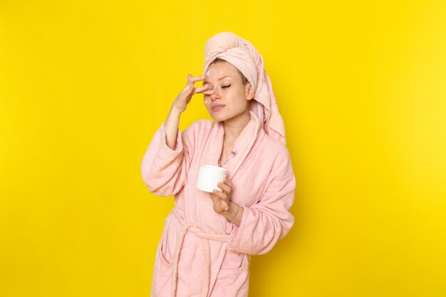 A front view young beautiful female in pink bathrobe using cream