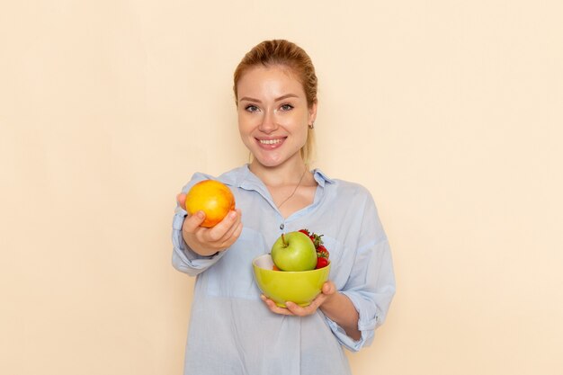 Front view young beautiful female in shirt holding plate with fruits on cream wall fruit model woman pose