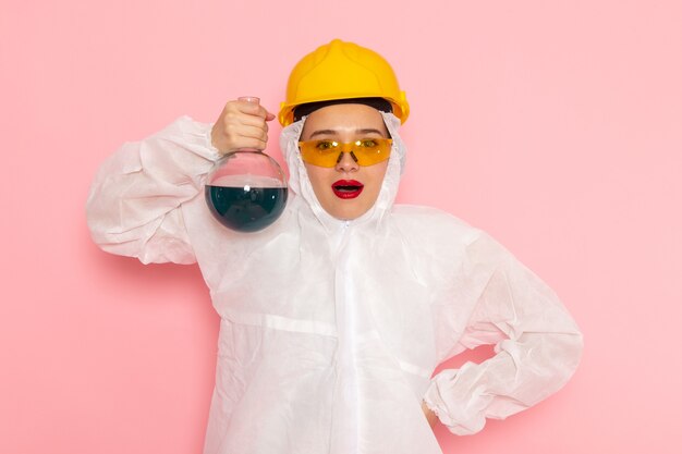 Front view young beautiful female in special white suit wearing protective helmet holding solution on the pink space special suit  woman