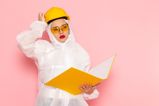 Front view young beautiful female in special white suit wearing protective helmet holding yellow file on the pink space special suit  woman