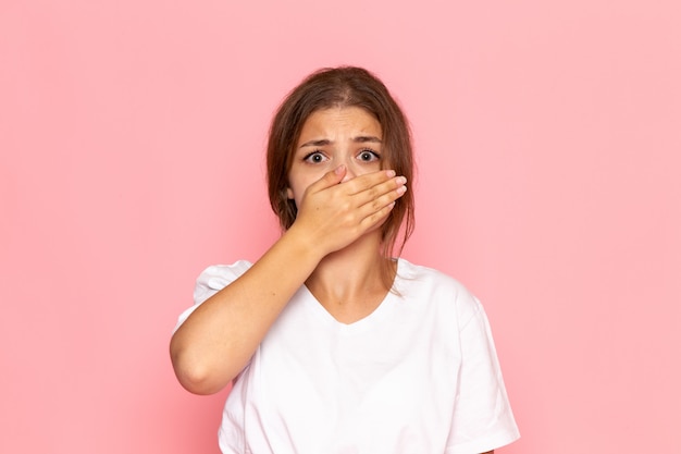 A front view young beautiful female in white shirt covering her face with scared expression
