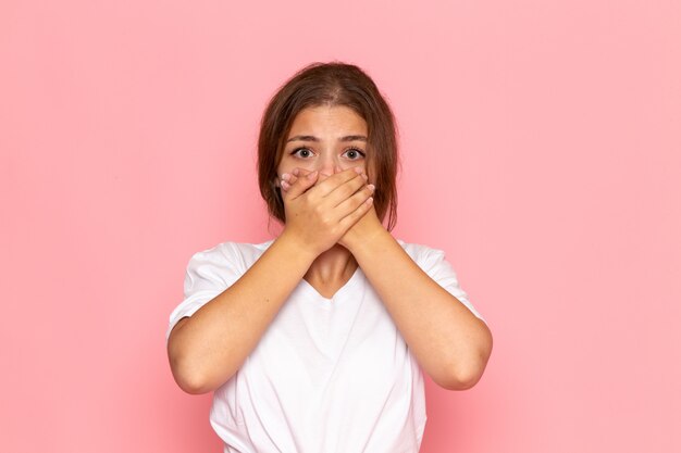 A front view young beautiful female in white shirt covering her mouth with scared expression