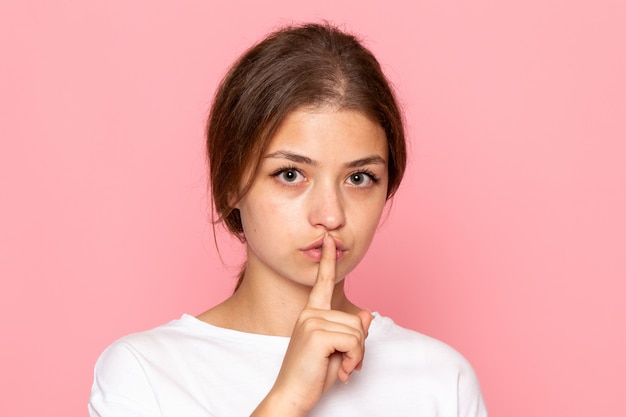 A front view young beautiful female in white shirt posing and showing silence sign