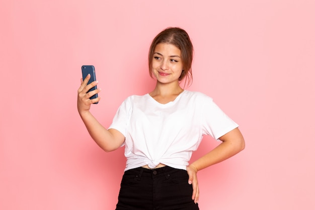 A front view young beautiful female in white shirt posing with funny expression and holding a phone