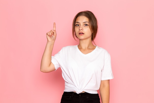 A front view young beautiful female in white shirt posing with raised finger