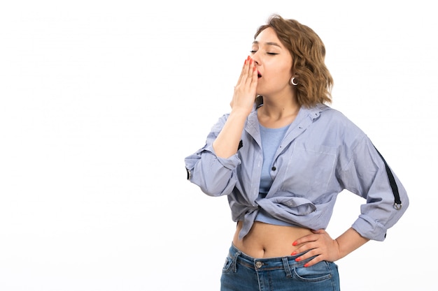 A front view young beautiful girl in blue shirt and blue jeans sneezing on the white