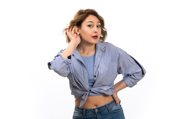 A front view young beautiful girl in blue shirt and blue jeans trying to hear out posing