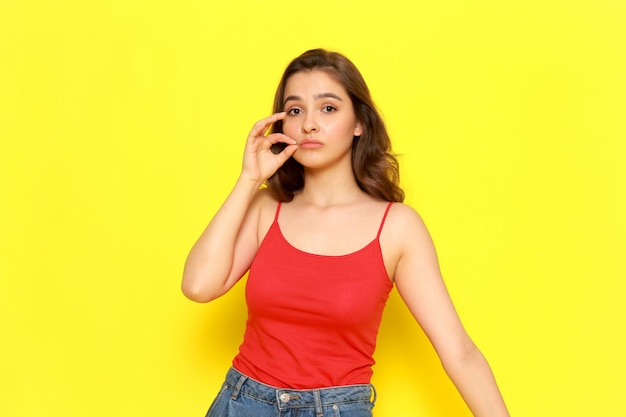 A front view young beautiful girl in red shirt and blue jeans closing her mouth