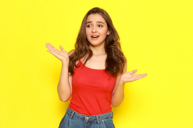 A front view young beautiful girl in red shirt and blue jeans posing with confused expression