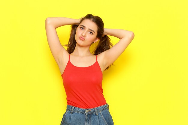 A front view young beautiful girl in red shirt and blue jeans posing with coquette expression