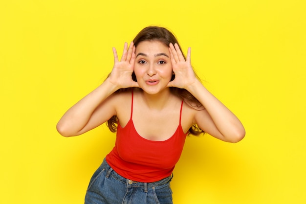 A front view young beautiful girl in red shirt and blue jeans posing with delighted expression