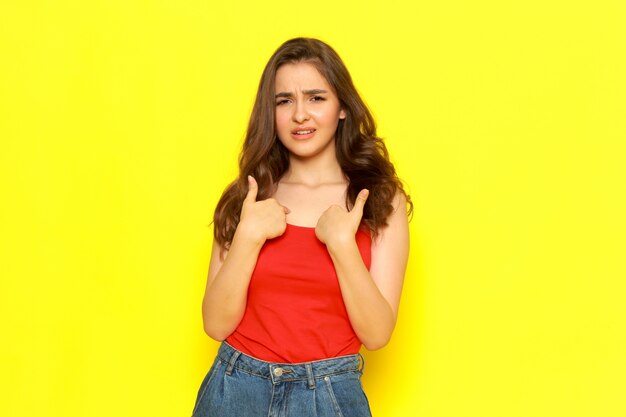 A front view young beautiful girl in red shirt and blue jeans posing with displeased expression