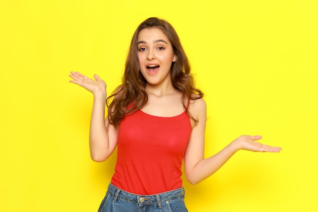 A front view young beautiful girl in red shirt and blue jeans posing with excited expression