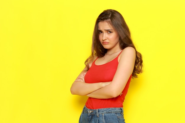 A front view young beautiful girl in red shirt and blue jeans posing with mad and saddened expression