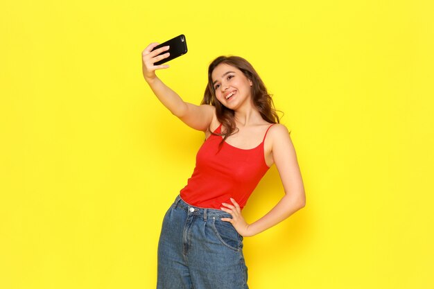 A front view young beautiful girl in red shirt and blue jeans taking a selfie