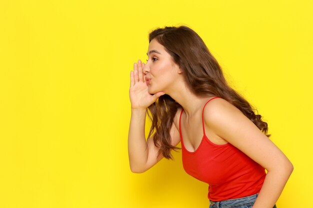 A front view young beautiful girl in red shirt and blue jeans whispering