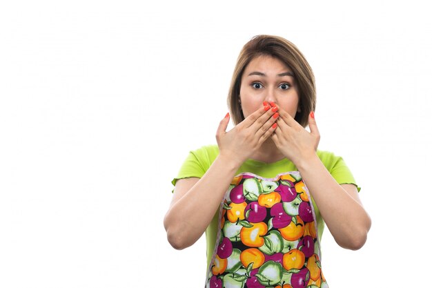 A front view young beautiful housewife in green shirt colorful cape covering her mouth with her hands shocked expression on the white background house female kitchen