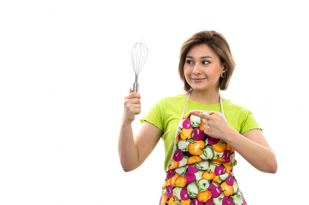 A front view young beautiful housewife in green shirt colorful cape holding kitchen appliance smiling on the white background house cleaning kitchen