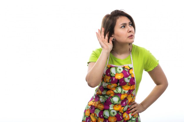 A front view young beautiful housewife in green shirt colorful cape trying to hear out