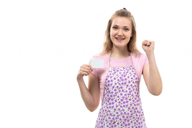 A front view young beautiful housewife in pink shirt colorful cape happy holding white card smiling